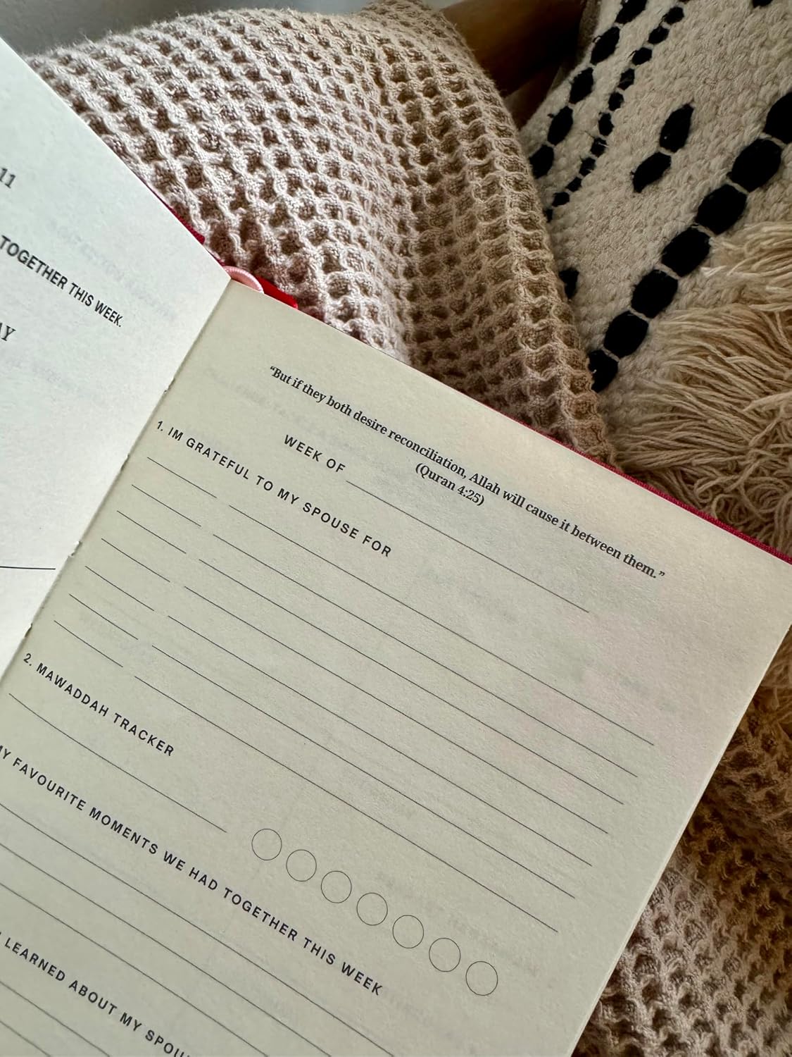 An open printed journal or planner page with lined writing areas and reflective prompts, placed on a beige knit blanket with a black-and-beige patterned textile nearby.