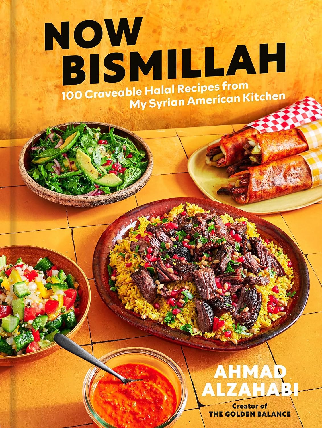 Book cover of 'Now Bismillah: 100 Craveable Halal Recipes from My Syrian American Kitchen' by Ahmad Alzahabi, featuring a warm orange background with large black title text and a table of prepared dishes including rice with meat, salads, and wraps.