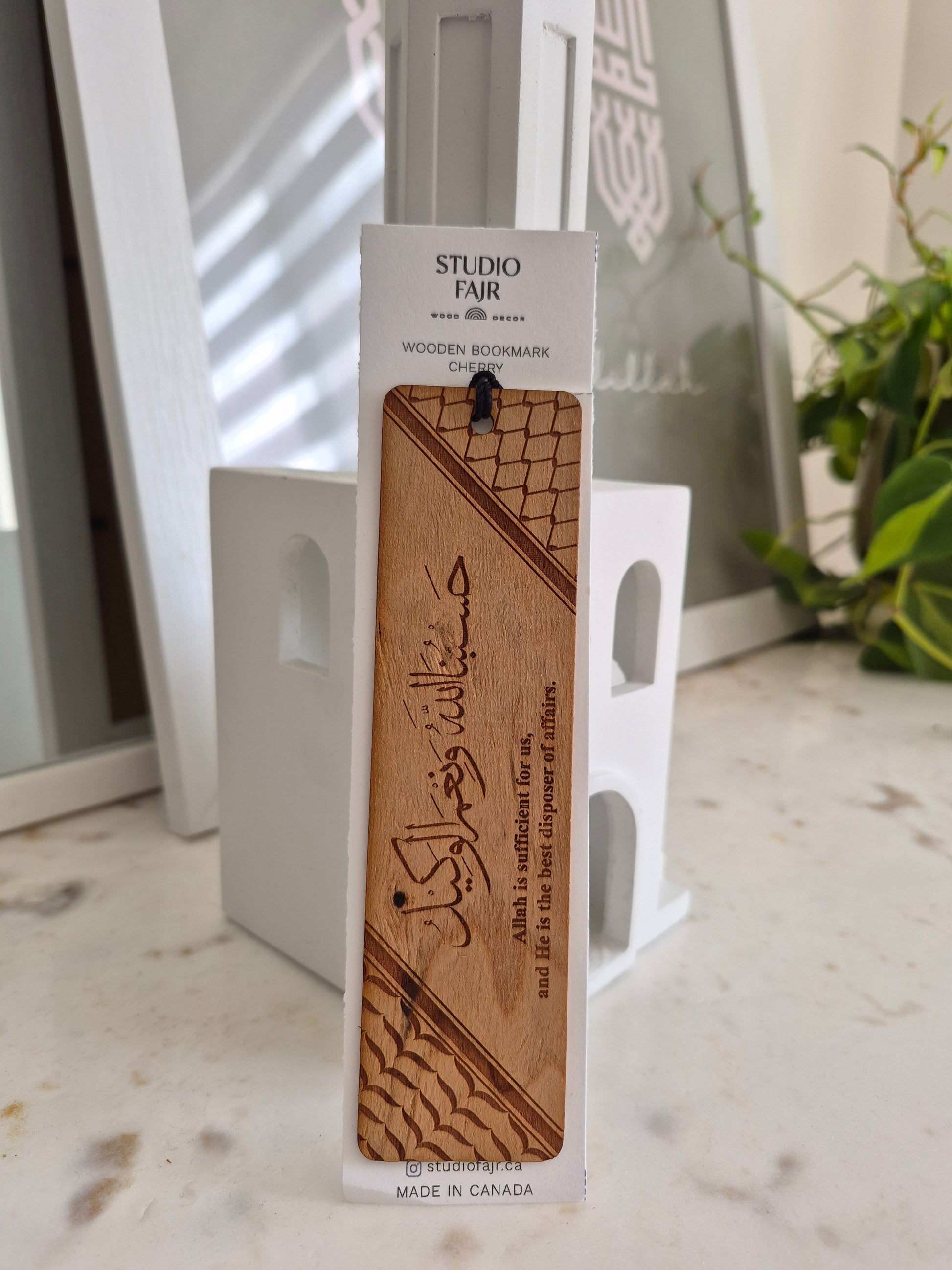 Wooden bookmark with engraved text on a white card, placed on a glass surface with a plant in the background.